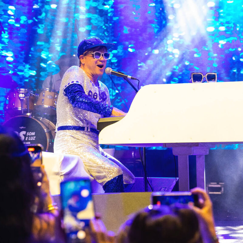 Elton John Cover - Maestro Rogério Martins no centro do palco com público ao fundo