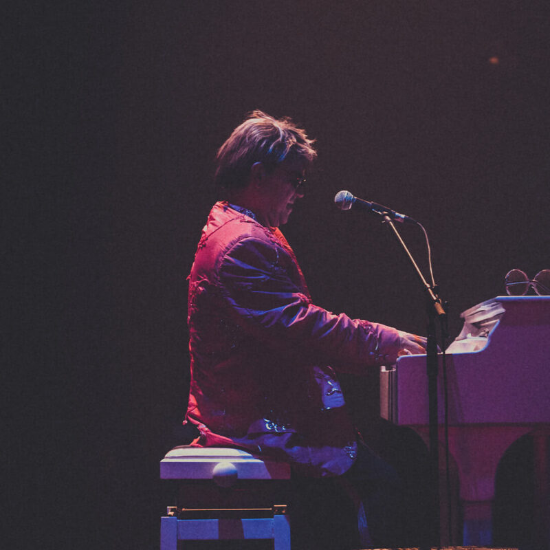 Maestro Rogério Martins em performance no show Your Song com terno vermelho.